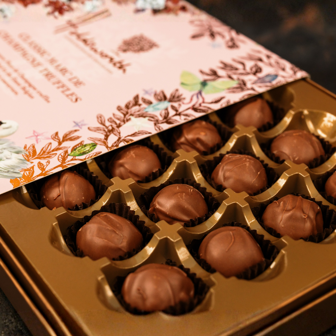 Gold box of chocolates with a decorative pink lid featuring floral designs.